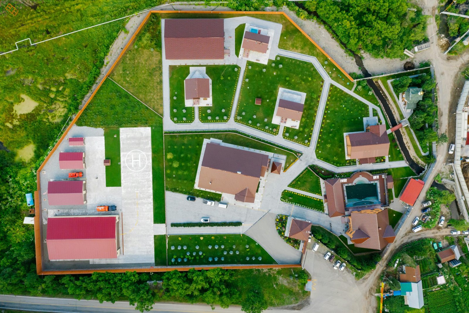 Aerial view of modern residential area with helipad, surrounded by greenery.